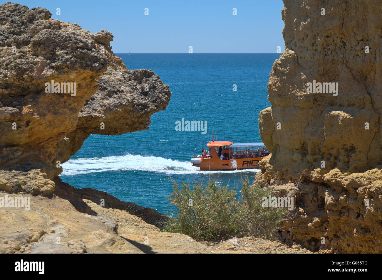 Barco turístico visitando los acantilados y cuevas cerca de la playa de Albandeira, una atracción popular entre los turistas durante la temporada de verano. Foto de stock