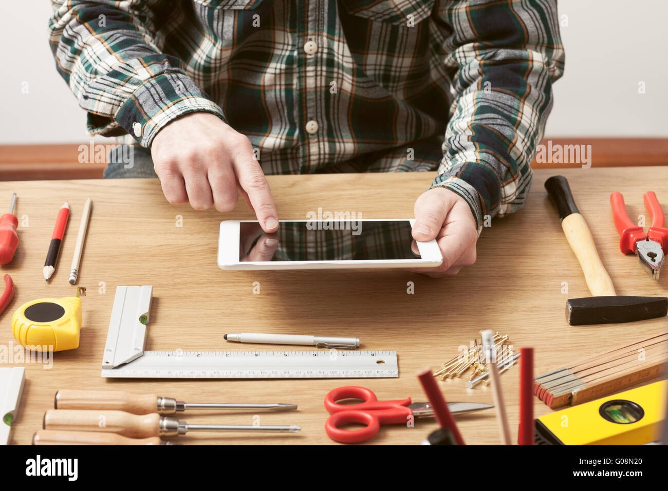Hombre trabajando en un proyecto de bricolaje en casa con una tableta digital, carpintería y herramientas de construcción sobre una mesa de trabajo, cerrar las manos arriba Foto de stock