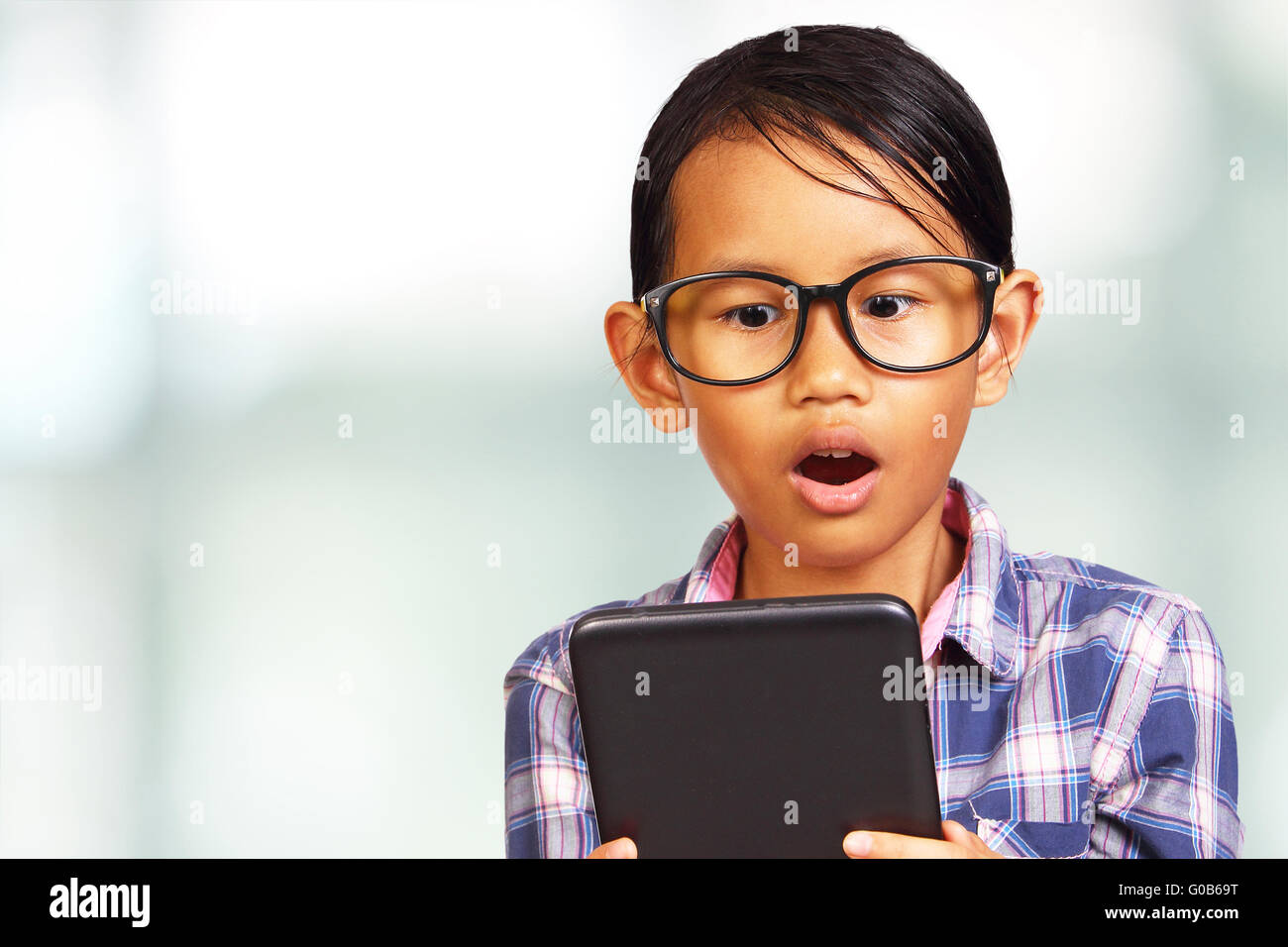 Joven asiática consternado mirando su tablet sobre fondo brillante Foto de stock