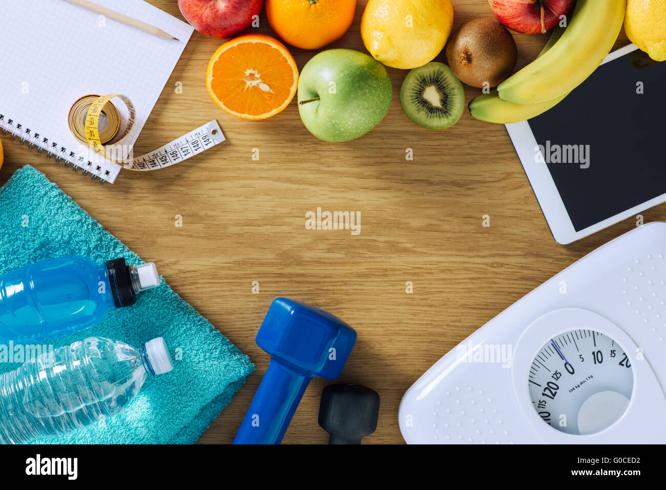 Concepto de Fitness y pérdida de peso, pesas, escala, toallas blancas, fruta, cinta métrica y tableta digital sobre una tabla de madera Foto de stock