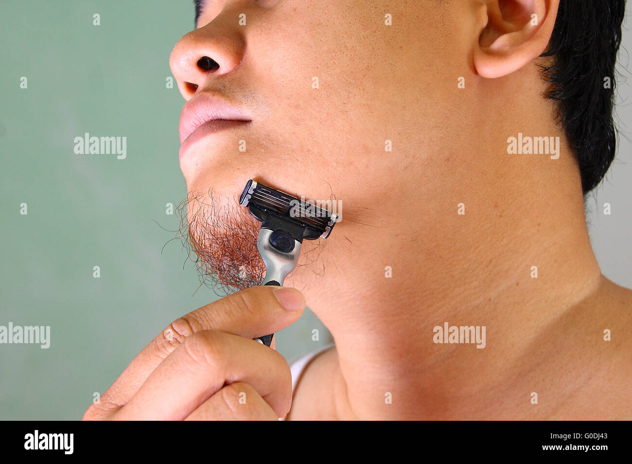Joven hombre asiático afeitar su vello facial sin crema Foto de stock