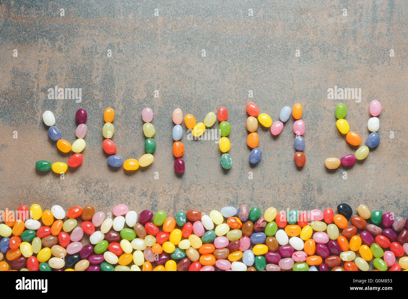Yummy palabra escrita con Jelly Beans, fondo oscuro con borde colorido Foto de stock