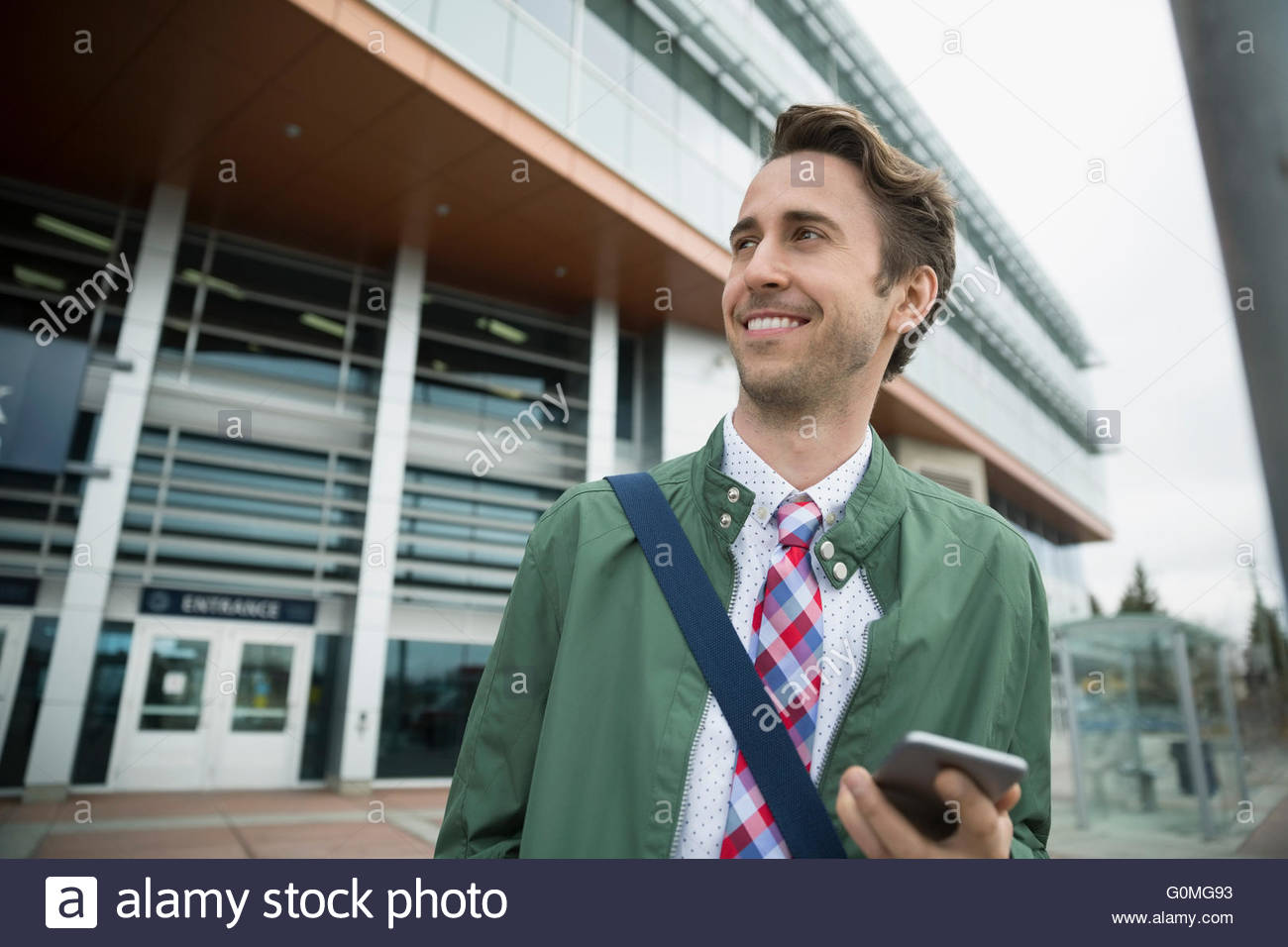 Empresario sonriente con teléfono móvil fuera de estación de tren Foto de stock