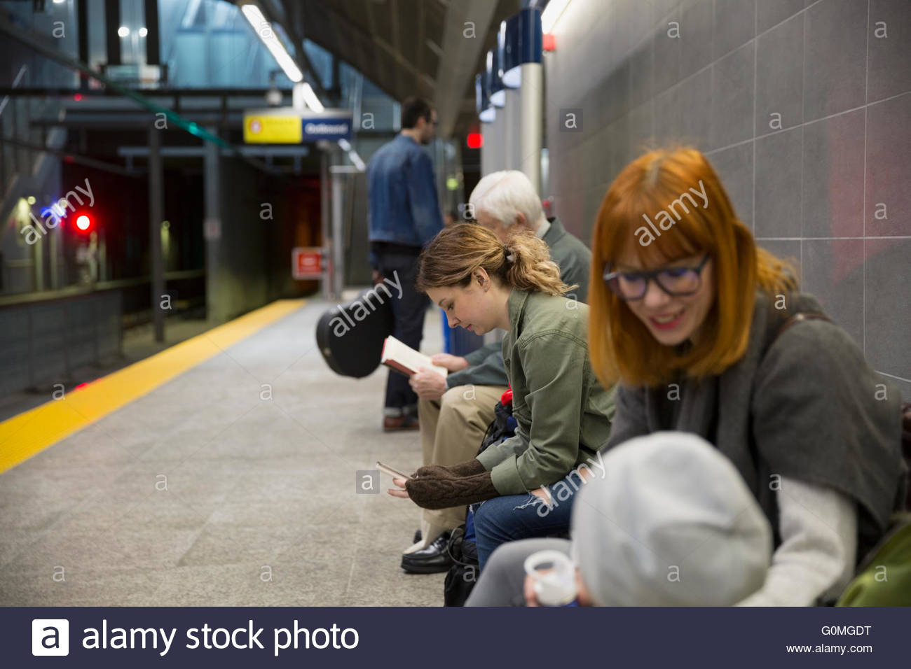 Gente esperando en un banco en la plataforma de la estación de metro Foto de stock