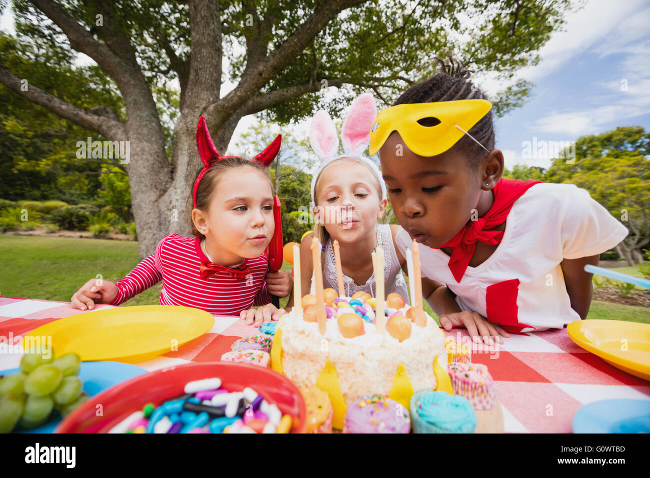 Tres pequeñas niñas soplando las velas de cumpleaños juntos Foto de stock