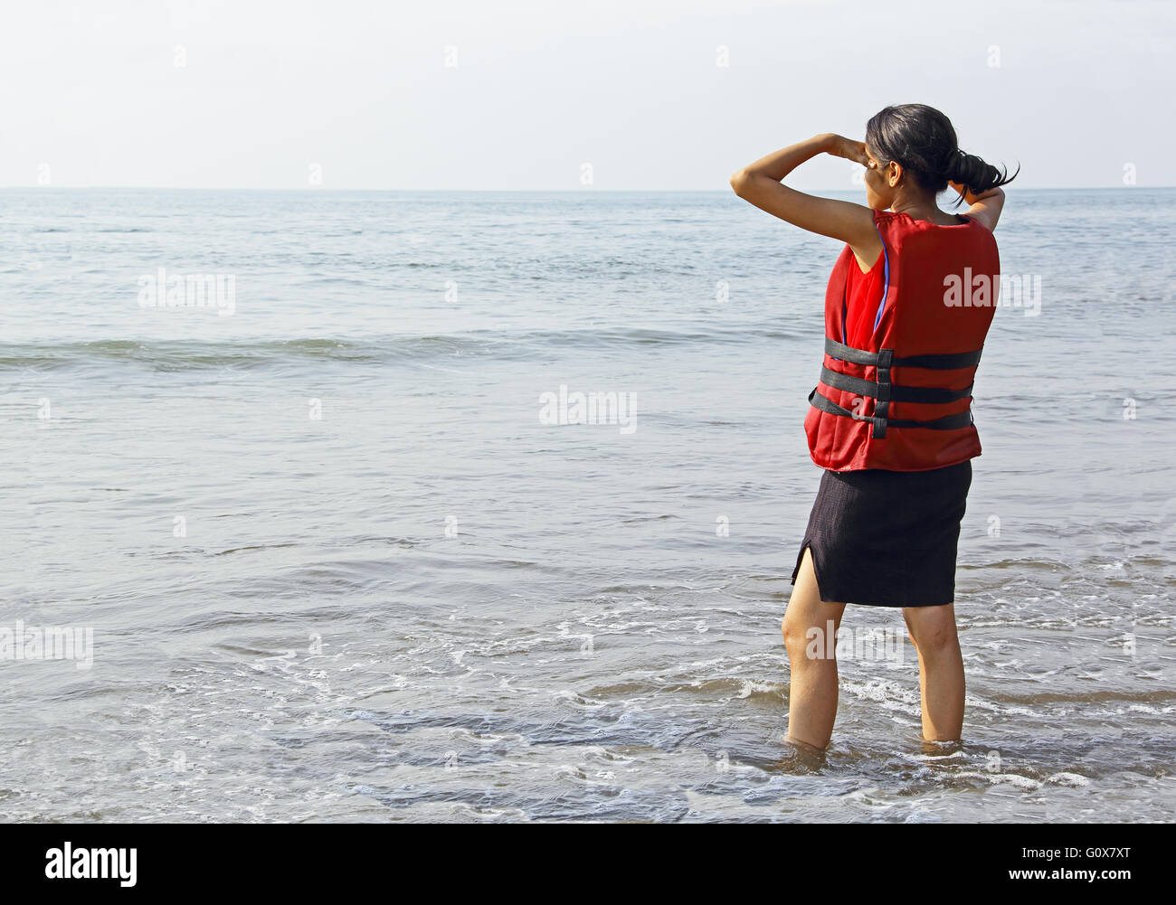 Jovencita en chaleco salvavidas esperando en la playa en Goa, India, preparado para actividades de deporte acuático Foto de stock