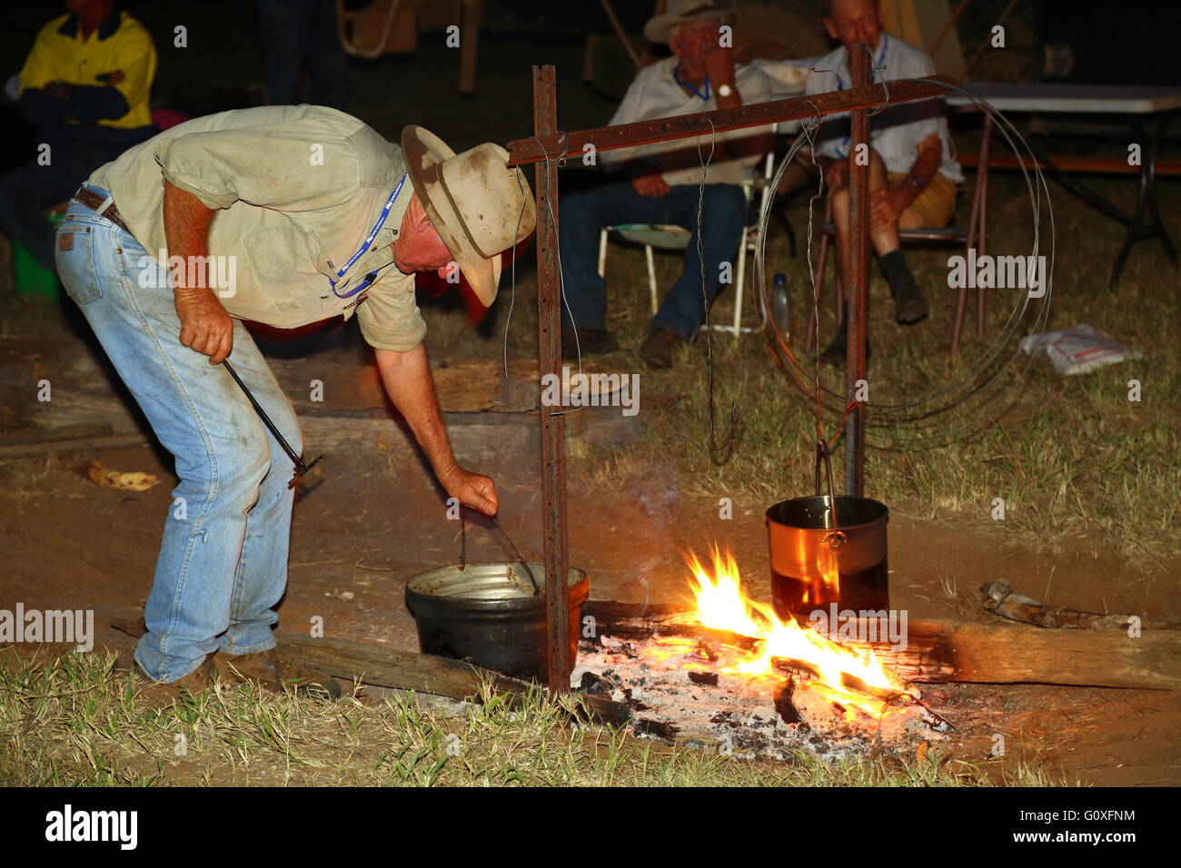 Un agricultor de mediana edad tiende a la olla de agua sobre un fuego de campamento en la zona rural de Australia. Foto de stock