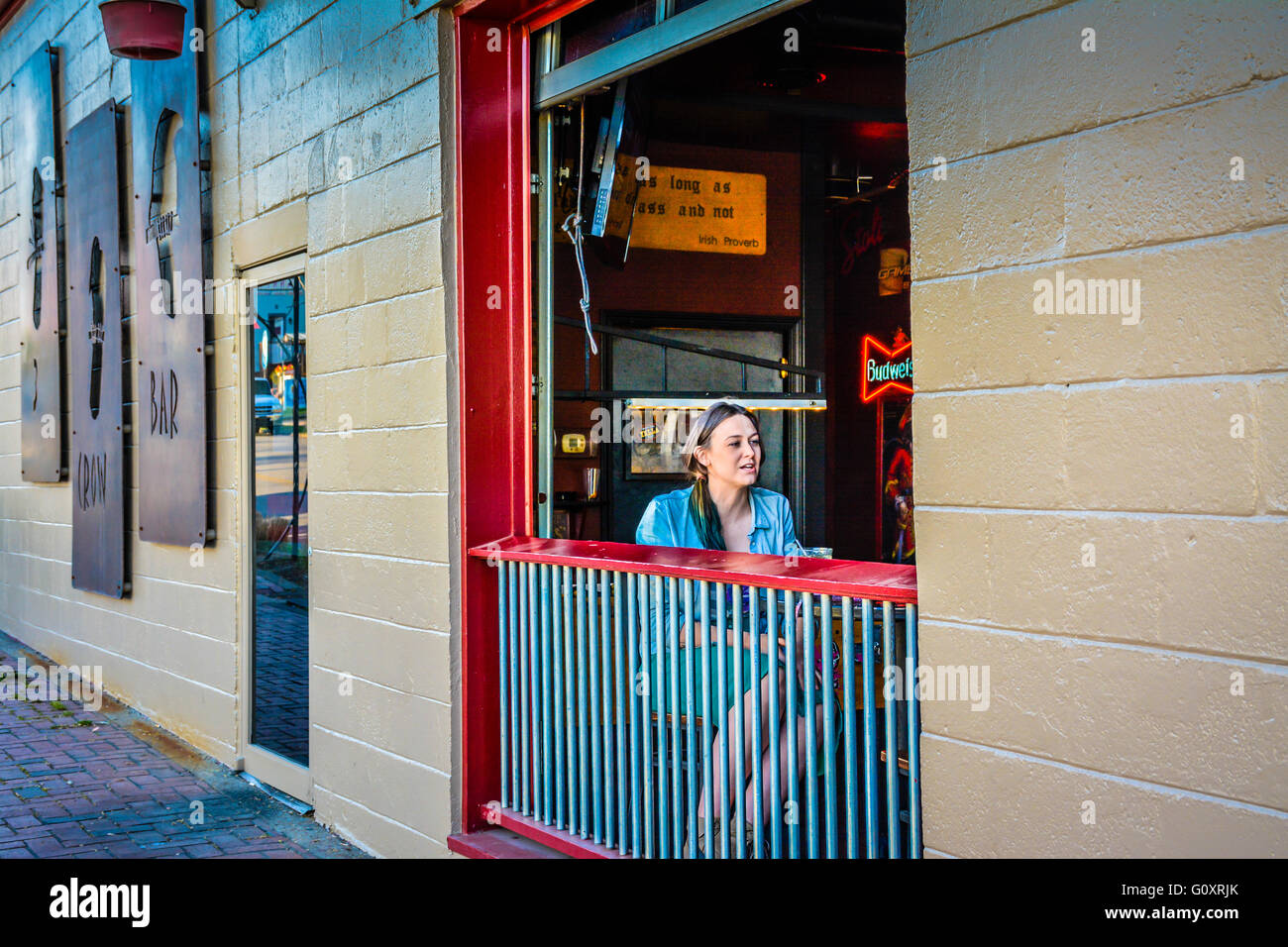 Una joven mujer sentada socializa en la mesa junto a la ventana abierta 3 Crow Bar en 5 puntos en el moderno distrito de East Nashville, TN Foto de stock