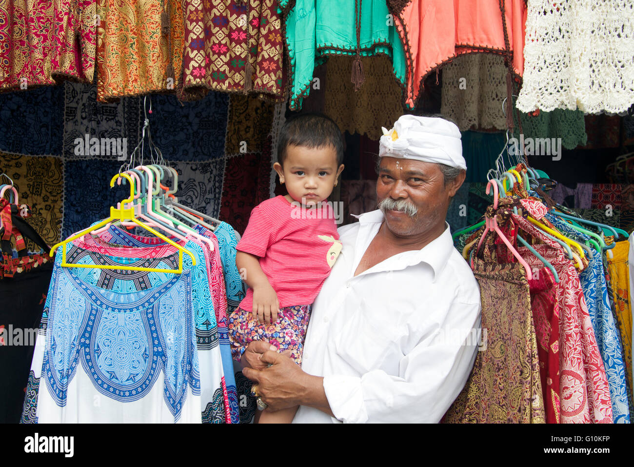 Dueño de la tienda de ropa mantiene su nieta Ubud, Bali, Indonesia Foto de stock
