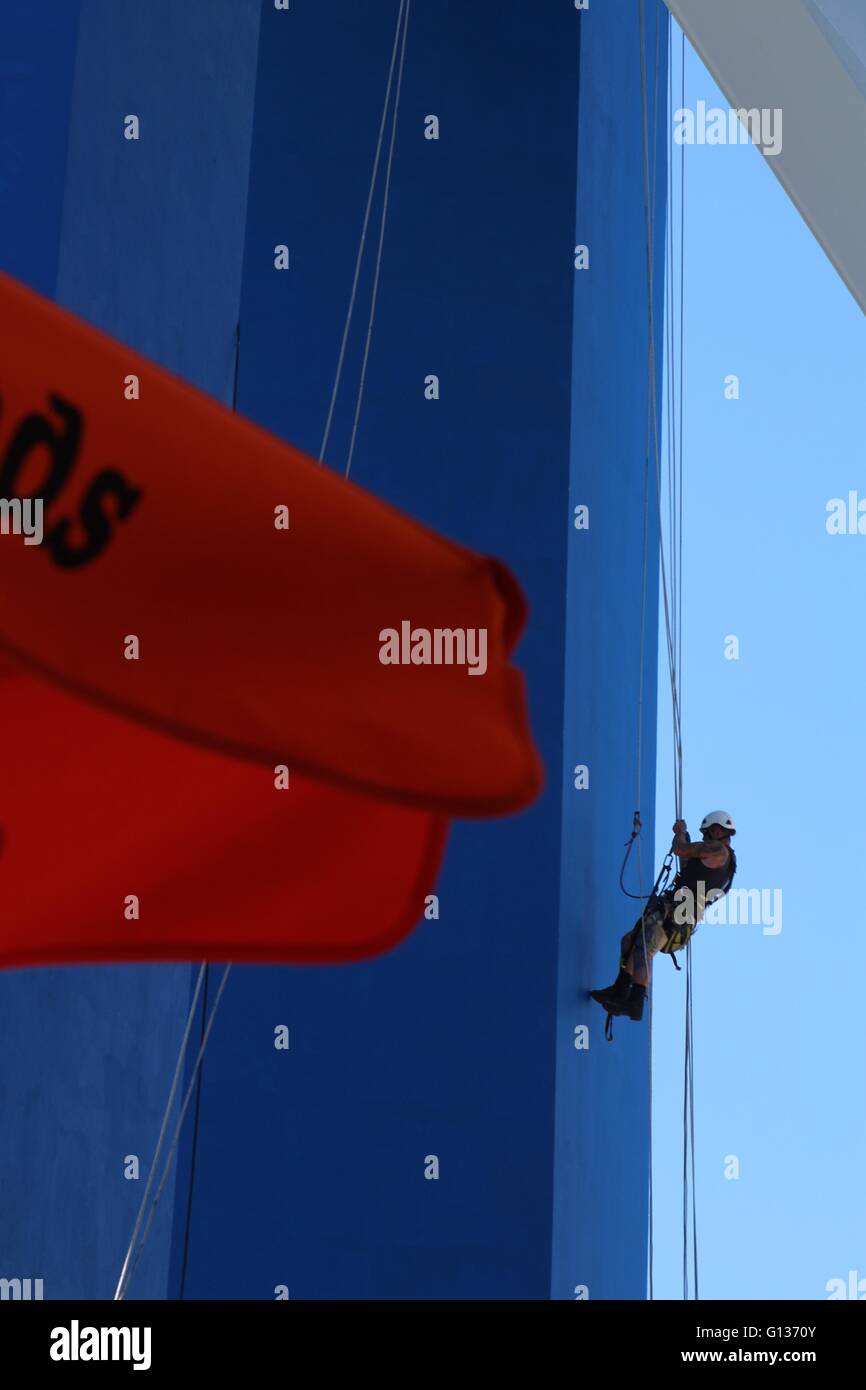 Persona vistiendo un sombrero duro rappel abajo una torre pintada de azul brillante con una vela roja en primer plano Foto de stock