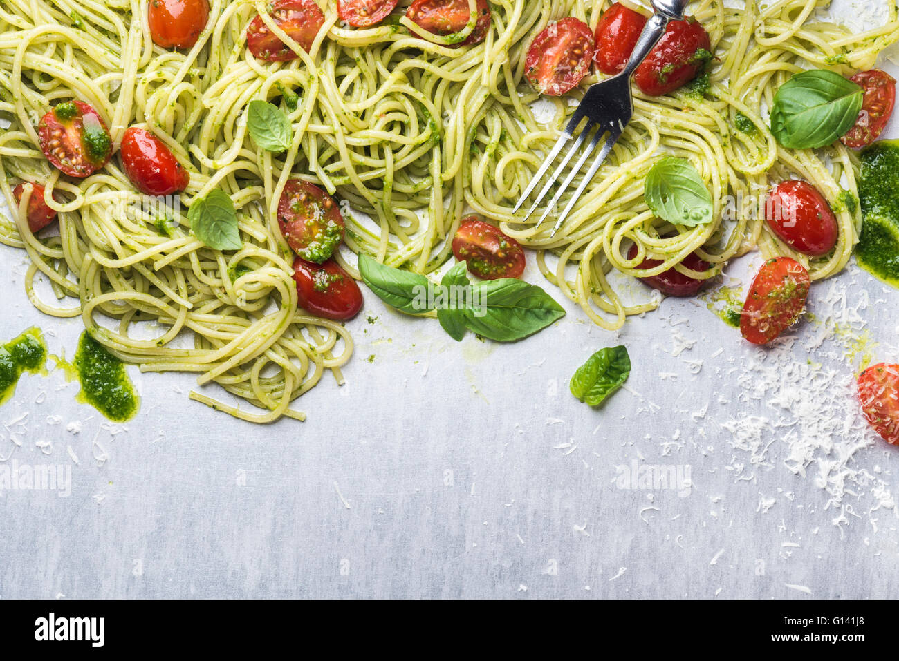 Espaguetis con salsa pesto, tomates cherry asados, albahaca fresca y queso parmesano sobre el telón de acero. Vista superior, espacio de copia Foto de stock