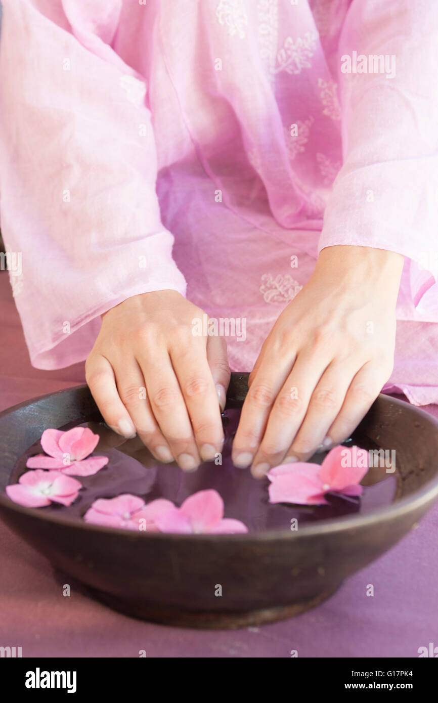 Captura recortada de una joven de las uñas en remojo en un tazón de agua pétalo de flor en spa Foto de stock