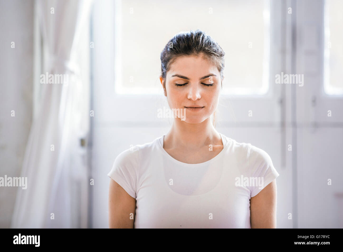 Joven mujer meditando con los ojos cerrados en el apartamento Foto de stock