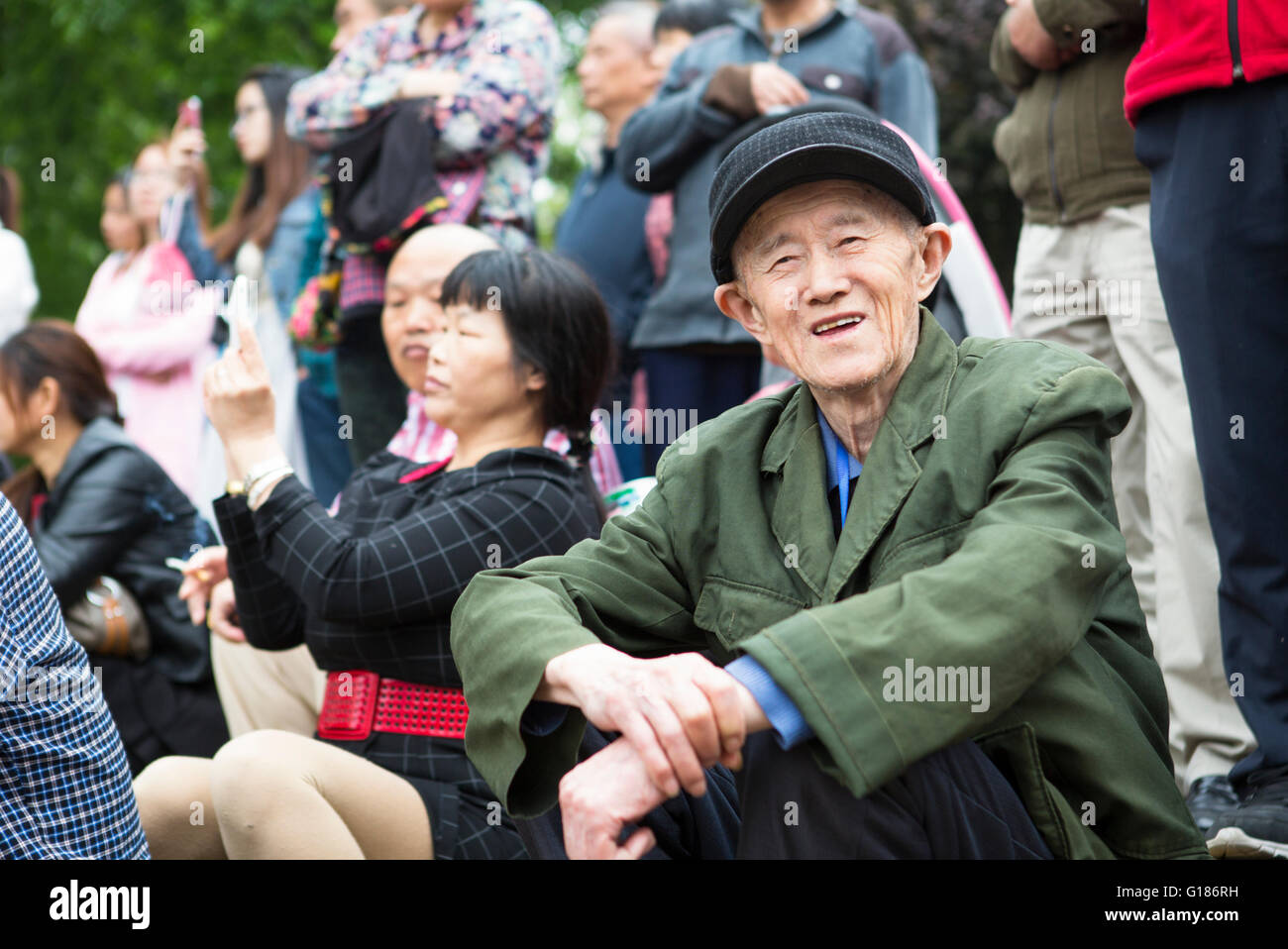 Retrato de un amable hombre chino sentado en la multitud con una camisa verde y un sombrero gris en el parque de Nanjing Foto de stock