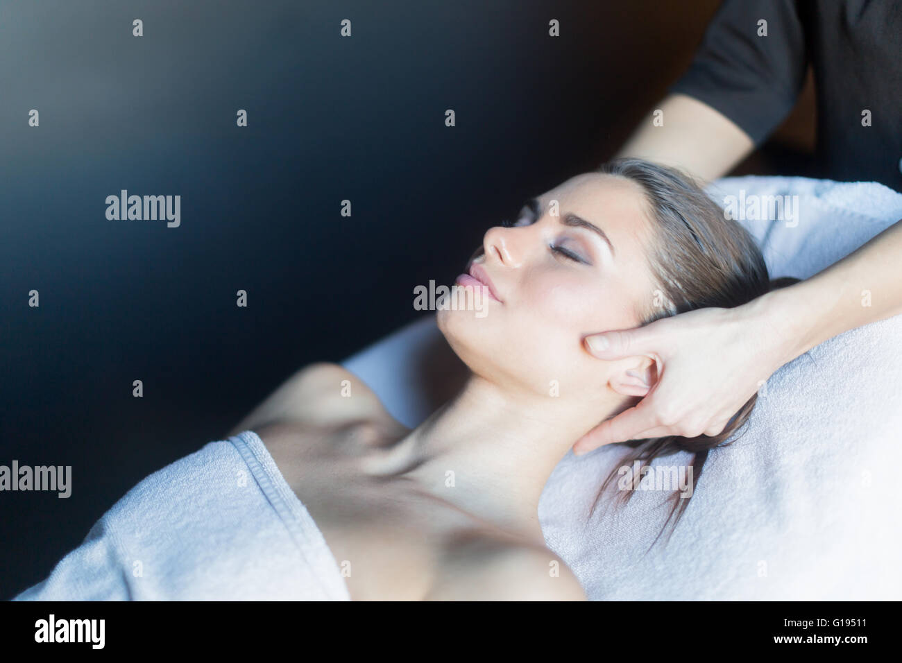 Masajista tratar cara de una hermosa joven tumbado en la mesa de masajes Foto de stock