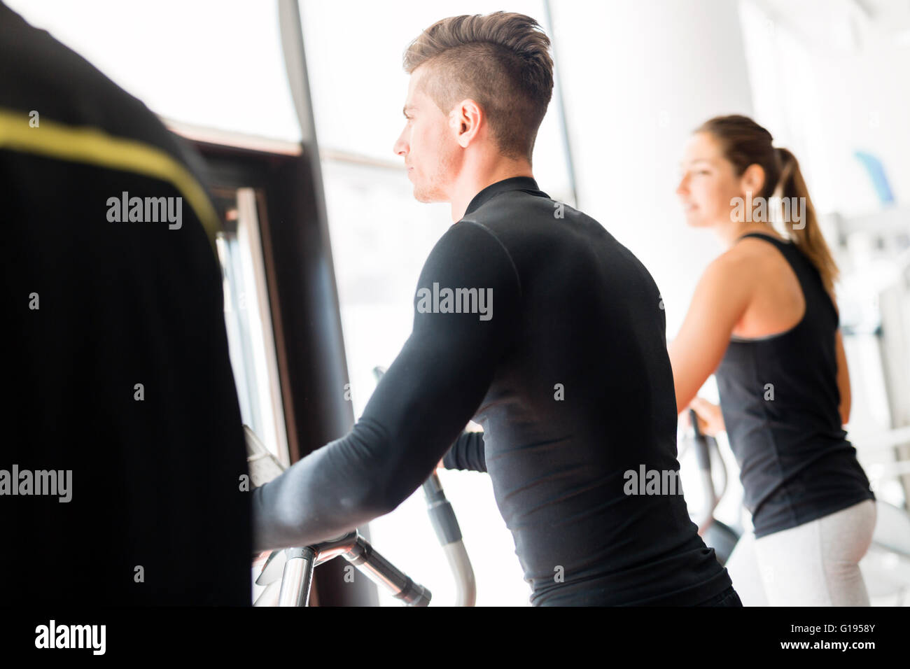 Grupo de personas jóvenes y sanos trabajaban sobre un entrenador elíptico en un gimnasio Foto de stock