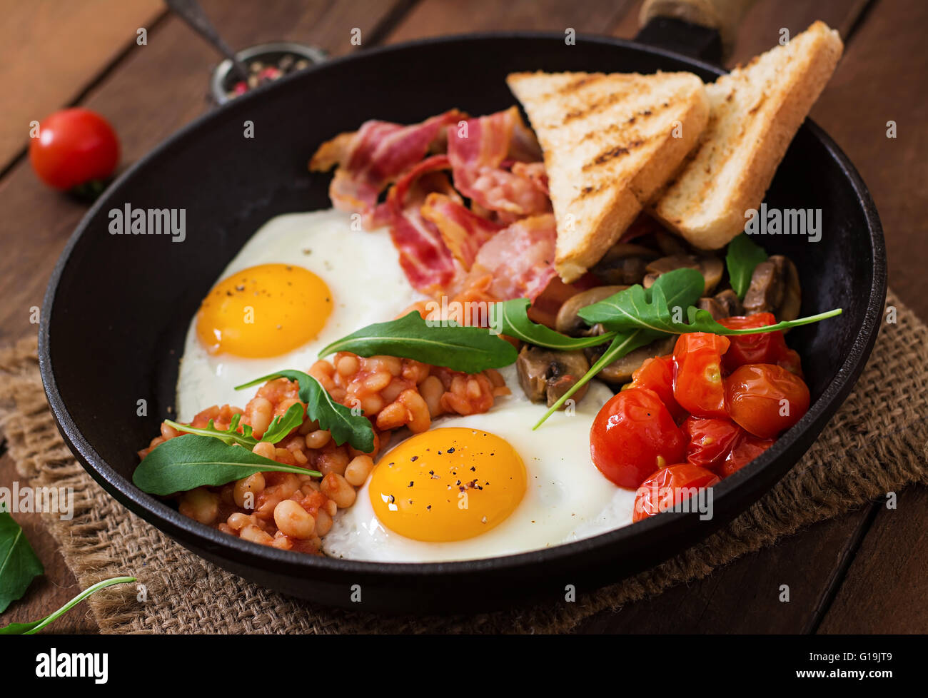Desayuno inglés, huevo frito, frijoles, tomates, champiñones, tocino y pan tostado Foto de stock