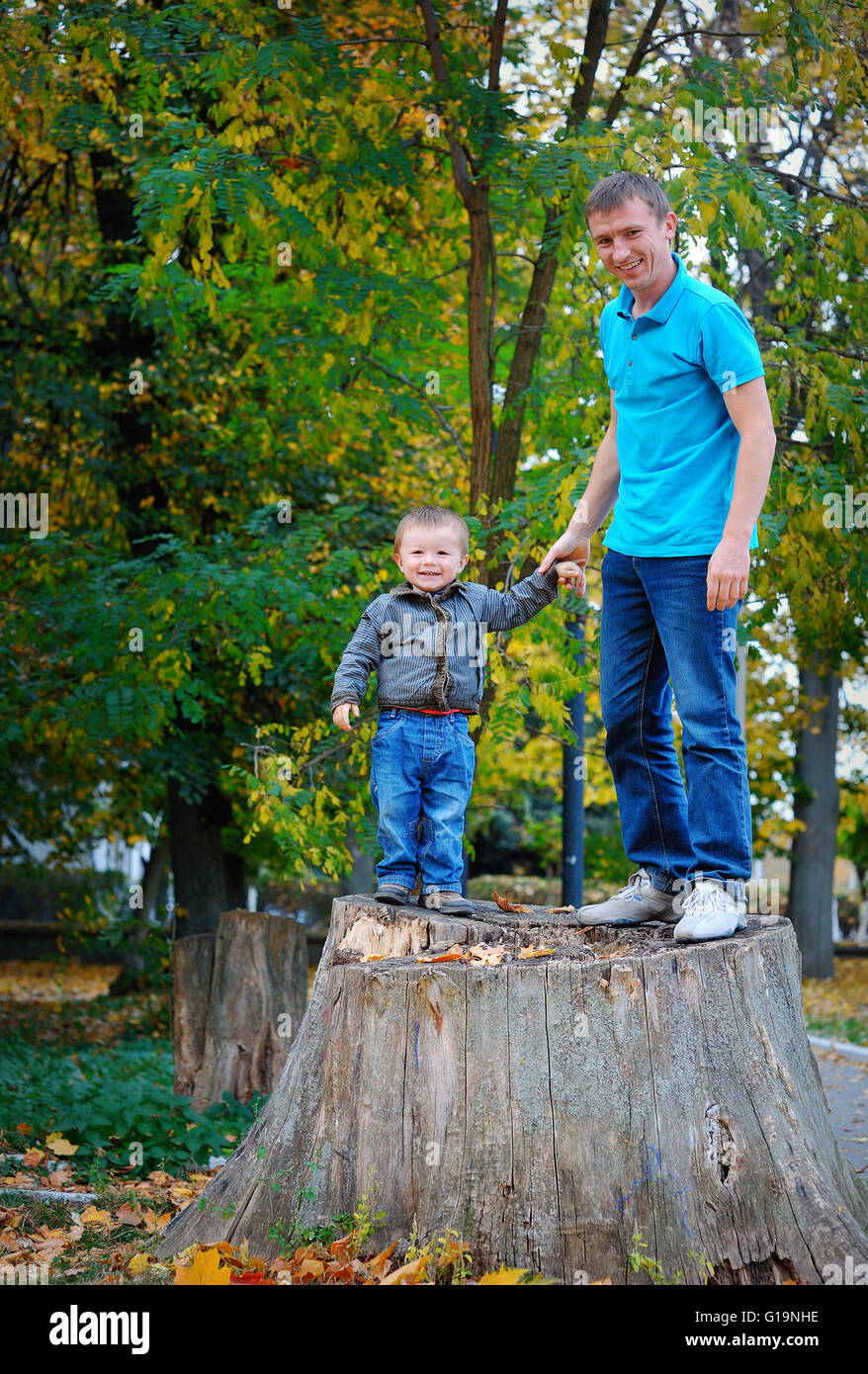 Padre e hijo de pie sobre un tocón en el parque Foto de stock
