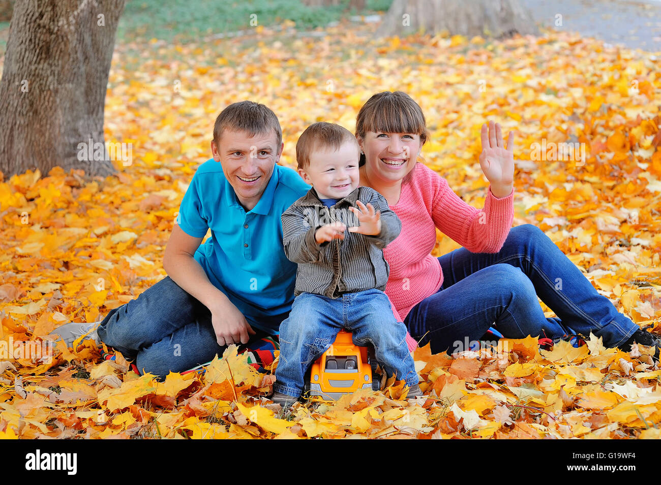 Familia Feliz, la madre, el padre y el hijo sentado en el otoño deja Foto de stock
