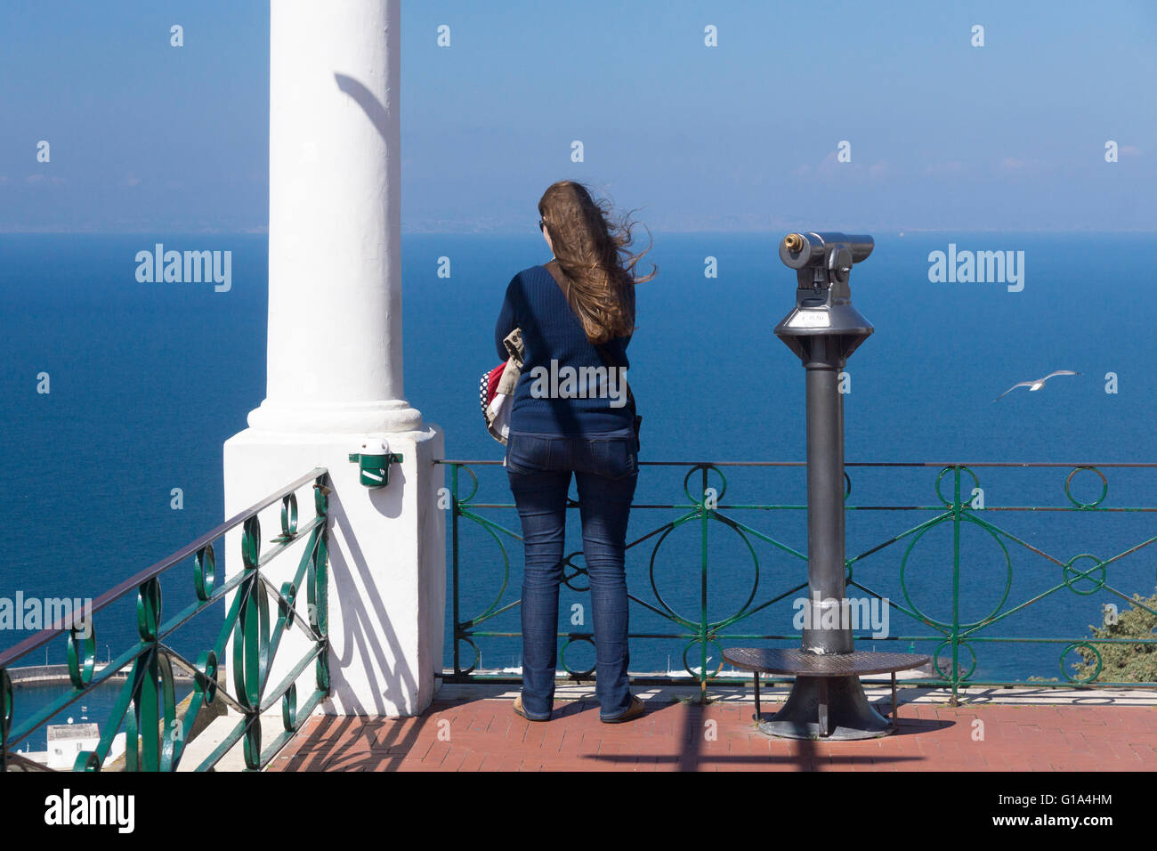 Una turista mujer parada en el borde de la Piazza Umberto I, mirando hacia el mar a través del Golfo de Nápoles. Marina Grande, Capri, Italia Foto de stock