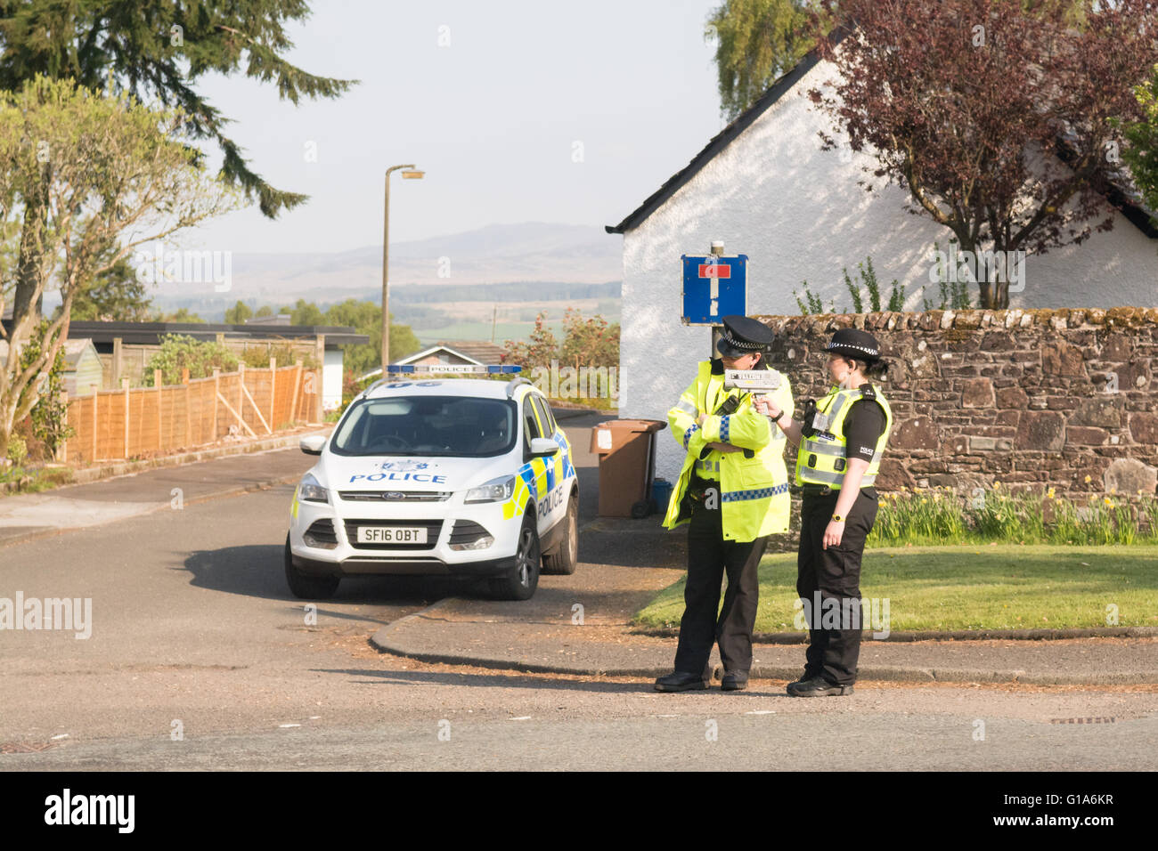 Hombres y mujeres policías con pistola de radar de mano en una aldea rural road en Killearn, Stirlingshire, Escocia, Reino Unido Foto de stock