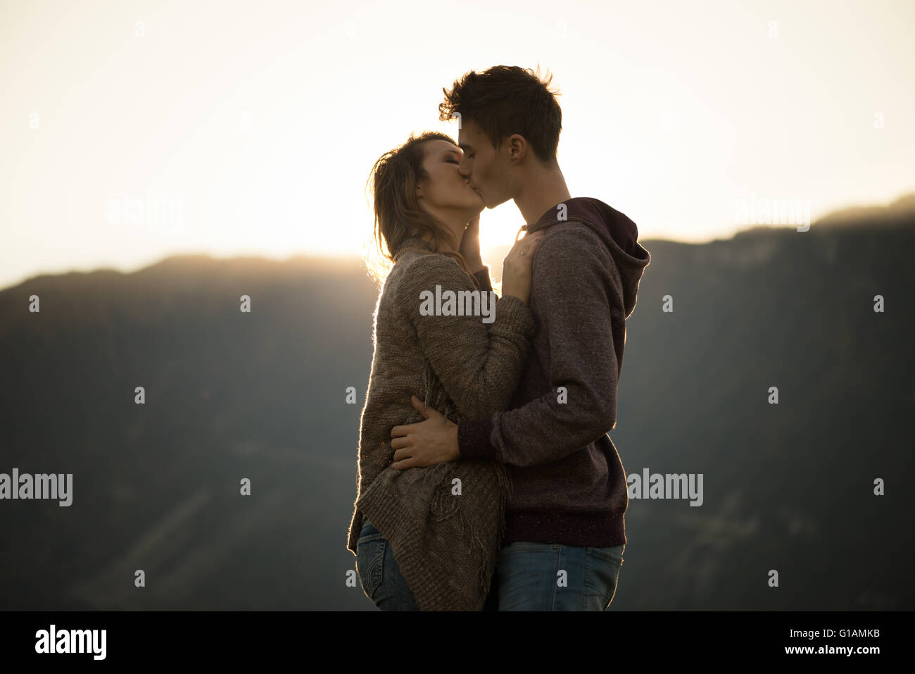 Romántico joven pareja besándose apasionadamente durante la puesta de sol, las montañas de fondo, sentimientos y relaciones concepto Foto de stock