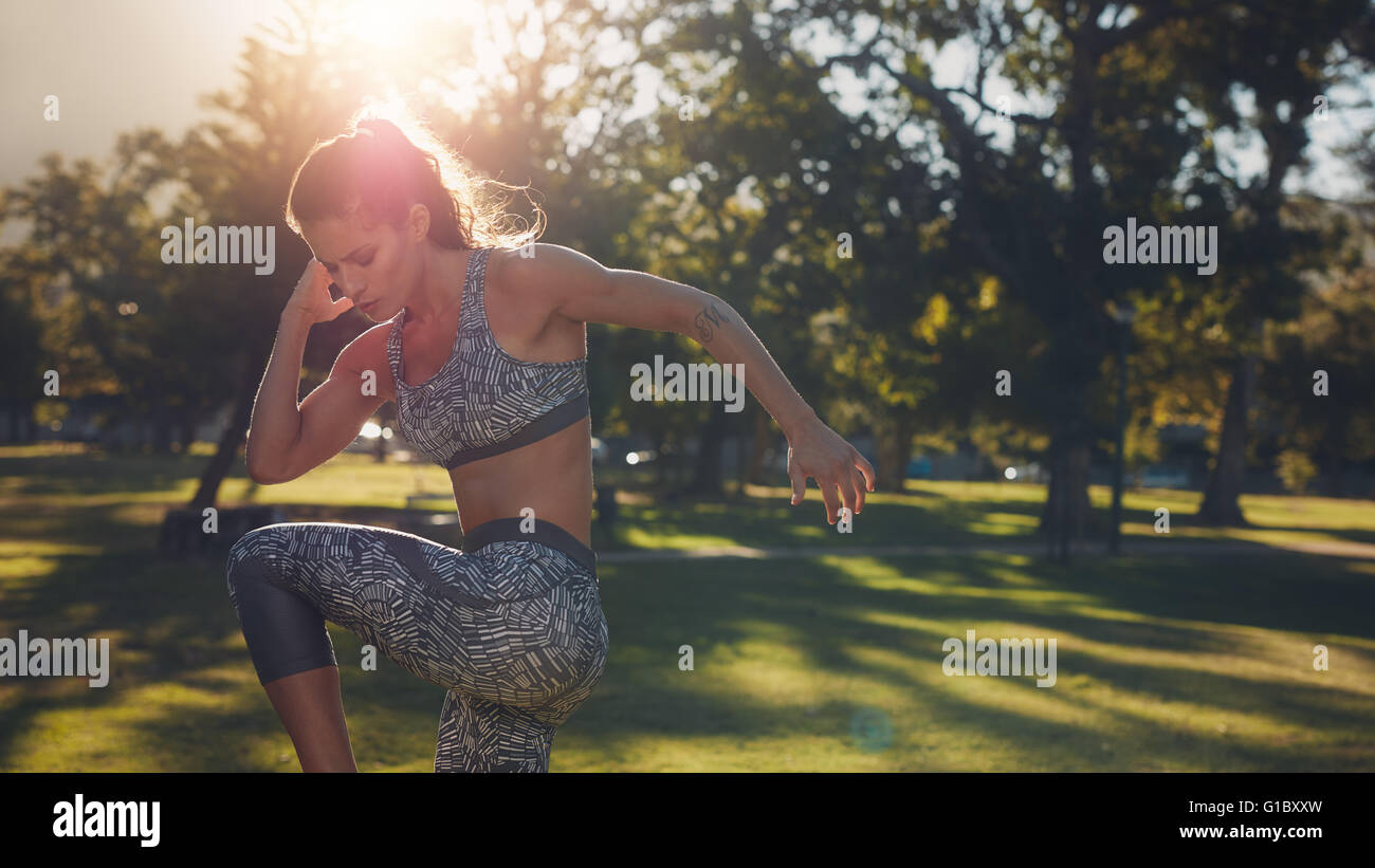 Disparó al aire libre de colocar joven haciendo ejercicios de calentamiento en el parque en un día soleado. Atleta Femenina estirando su cuerpo antes Foto de stock