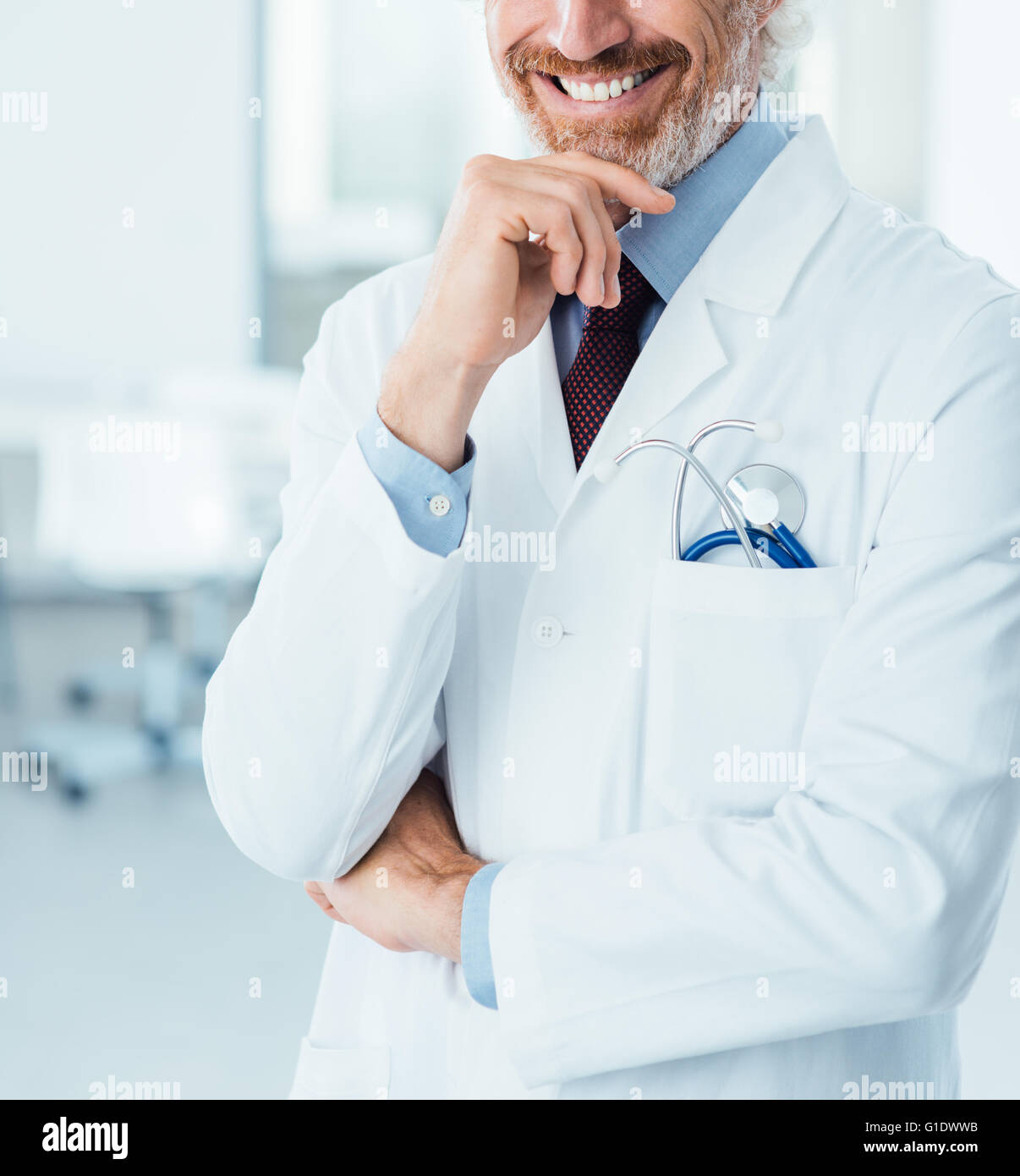 Profesional médico posando en el hospital y sonriendo a la cámara con la mano en la barbilla Foto de stock
