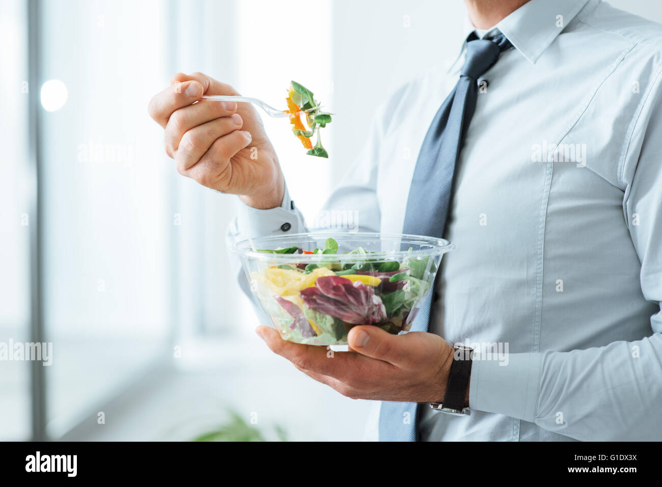 El empresario tiene una ensalada de verduras para comer, comer sano y el concepto de estilo de vida, persona irreconocible Foto de stock