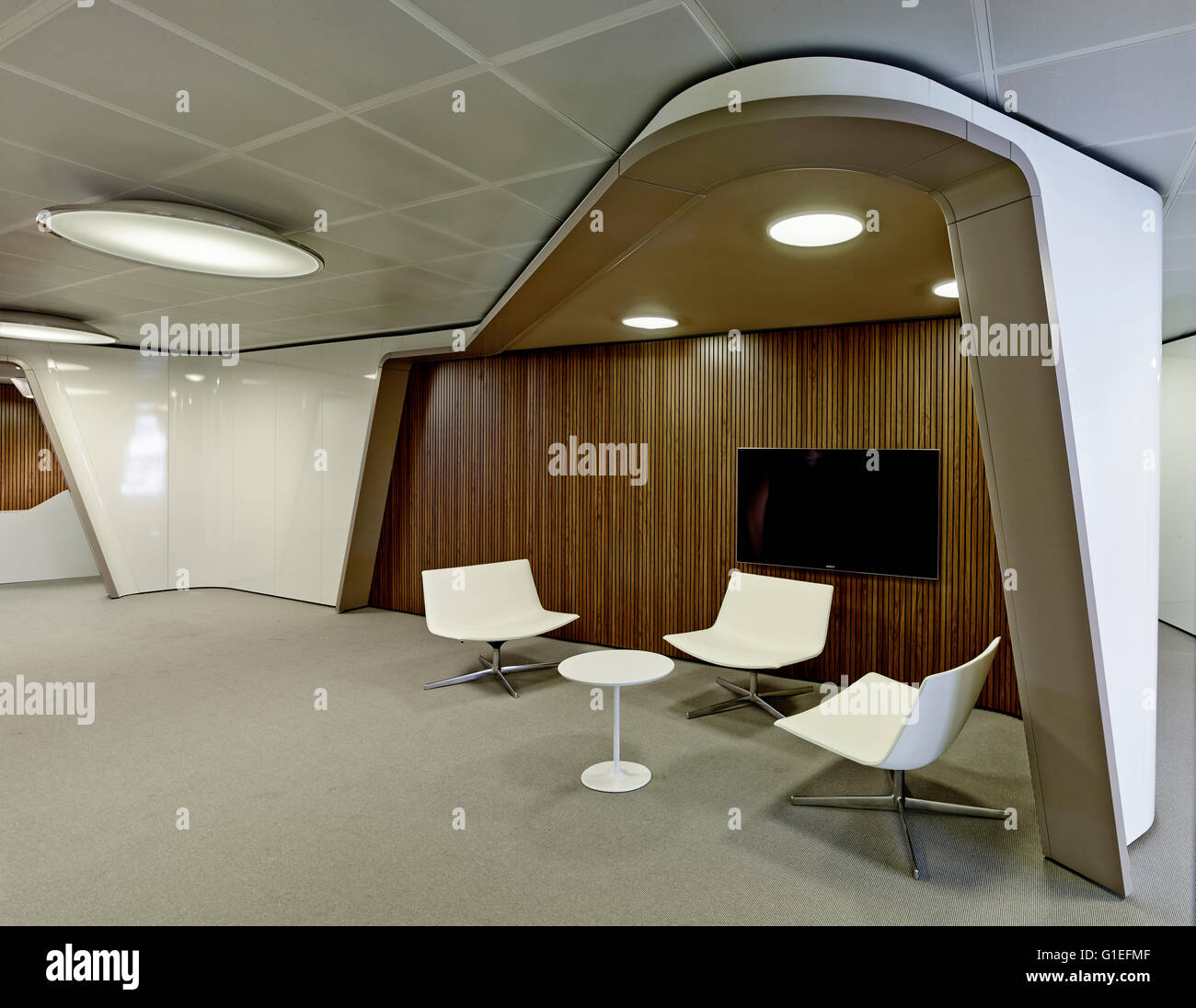 Oficinas inaugure, Barcelona, España. Espacio de trabajo con sillas modernas blanco bajo una curva en el techo. Paneles de madera en la pared con un televisor de pantalla plana. Foto de stock