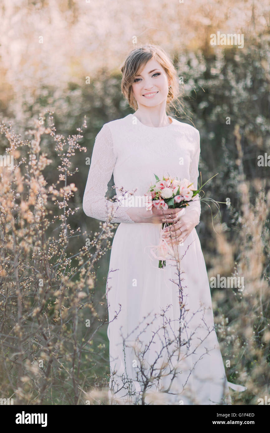 Hermosa joven rubia vestidos de novia vestido blanco con bouquet en la  floración en el prado. Disfruta de la naturaleza delicada niña primavera  Fotografía de stock - Alamy