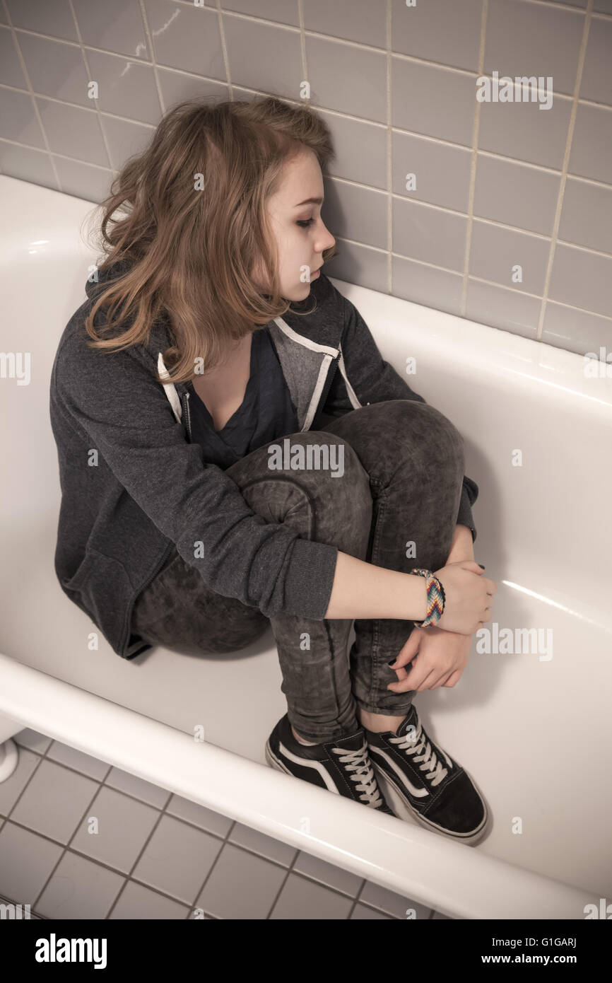 Subrayó triste rubia caucásica adolescente sentado en la bañera vacía. Retrato de estudio estilizados, corrección del filtro tonal, vintage styl Foto de stock