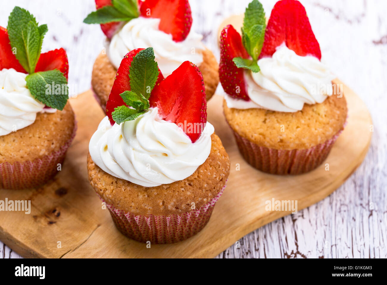Cupcakes buttercream casero con fresas y menta fresca sobre mesa de madera blanca Foto de stock