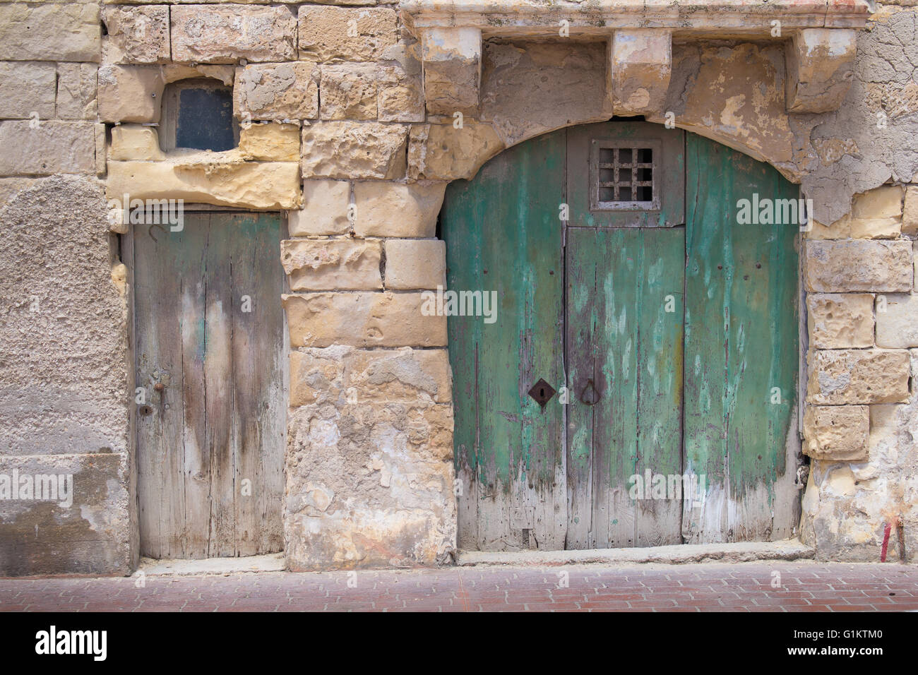 Calle de un antiguo pueblo de pescadores en la isla de Malta, de Marsaxlokk. Viejo verde grande puerta con un arco pequeño y tradicional. Construcción Foto de stock