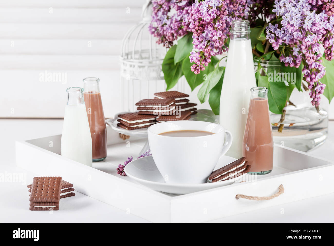 Taza de café y unas cuantas botellas de leche y chocolate blanco miklshakes  en una bandeja con flores de color lila en persianas blancas antecedentes  Fotografía de stock - Alamy