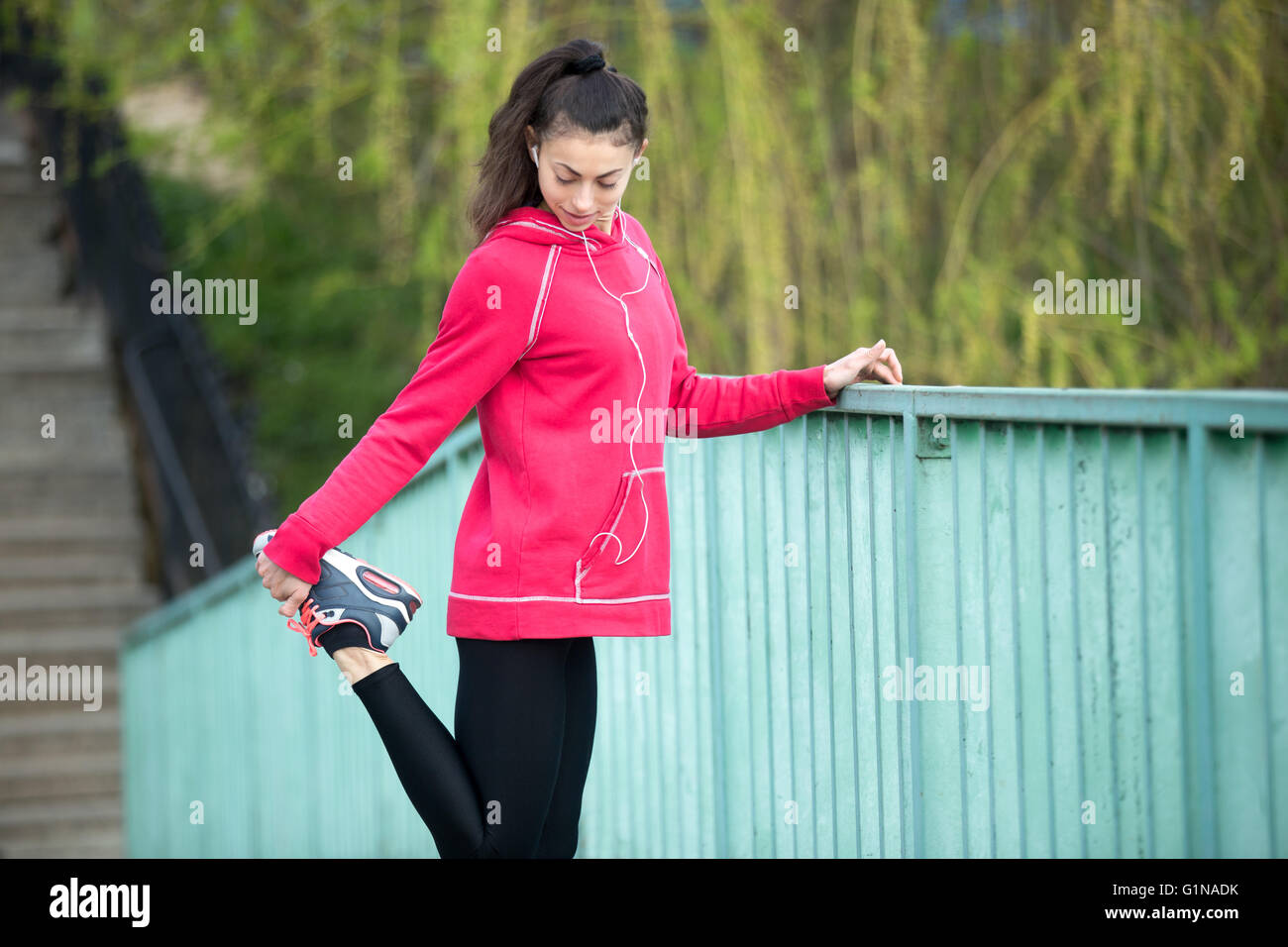 Retrato de mujer deportiva haciendo ejercicios de estiramiento en el parque antes de la capacitación. Atleta Femenina runner escuchando música mientras te Foto de stock