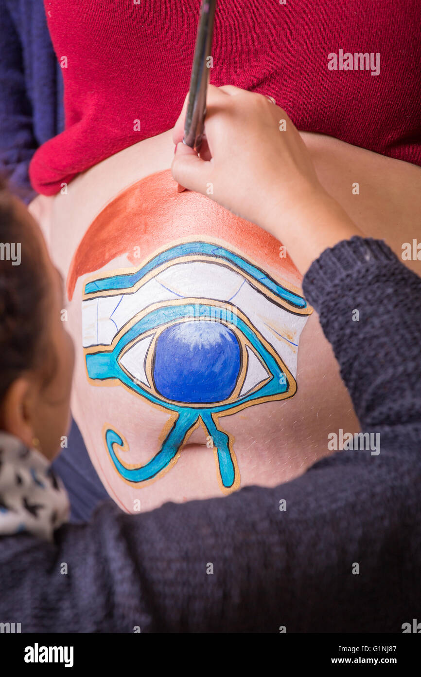 Arte del cuerpo maquillaje artista crear Ojo de Horus pintando en el vientre de una mujer embarazada Foto de stock
