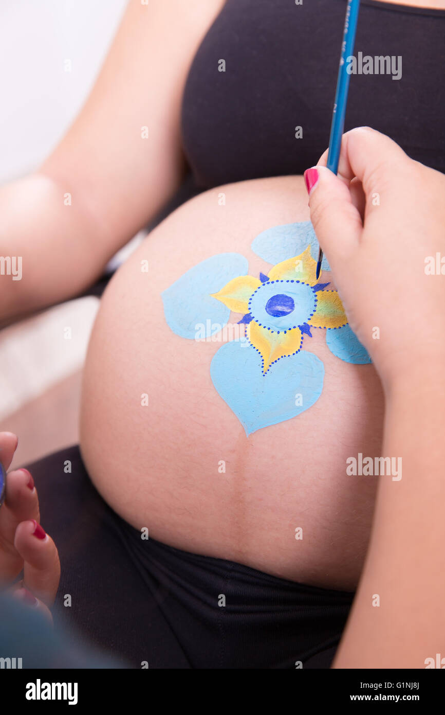 Arte del cuerpo maquillaje artista pintando en el vientre de una mujer joven embarazada Foto de stock