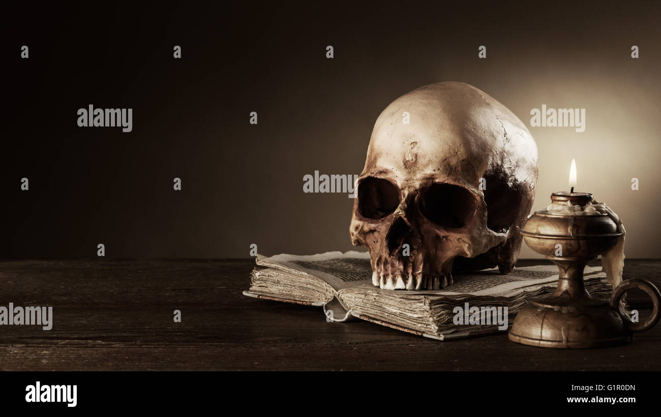Cráneo humano, vela y antiguo libro abierto sobre una mesa de madera antigua, el conocimiento y el concepto de alfabetización Foto de stock