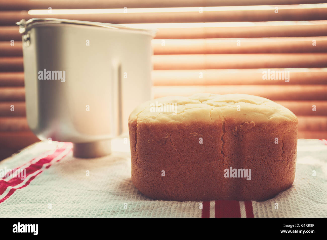Una hogaza de pan recién horneado y una panificadora de estaño por la ventana bañado por los rayos del sol Foto de stock