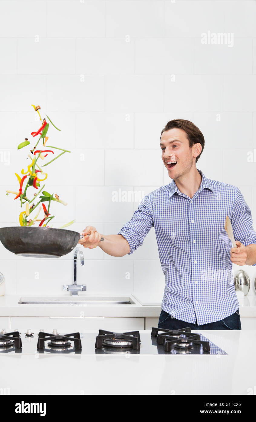 Sorprendido par cocinar verduras y voltear en la sartén en la cocina Foto de stock