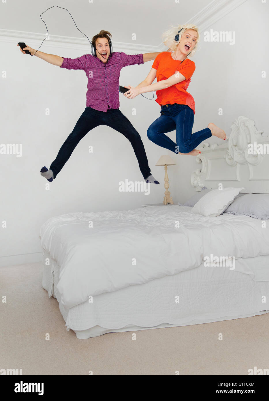 Retrato pareja juguetona saltando sobre la cama y escuchar música con el reproductor de mp3 y auriculares Foto de stock