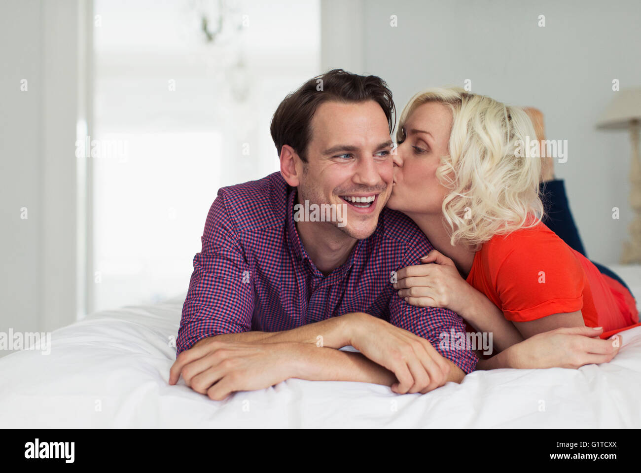 Esposa afectuoso beso sonriente marido en la cama Foto de stock