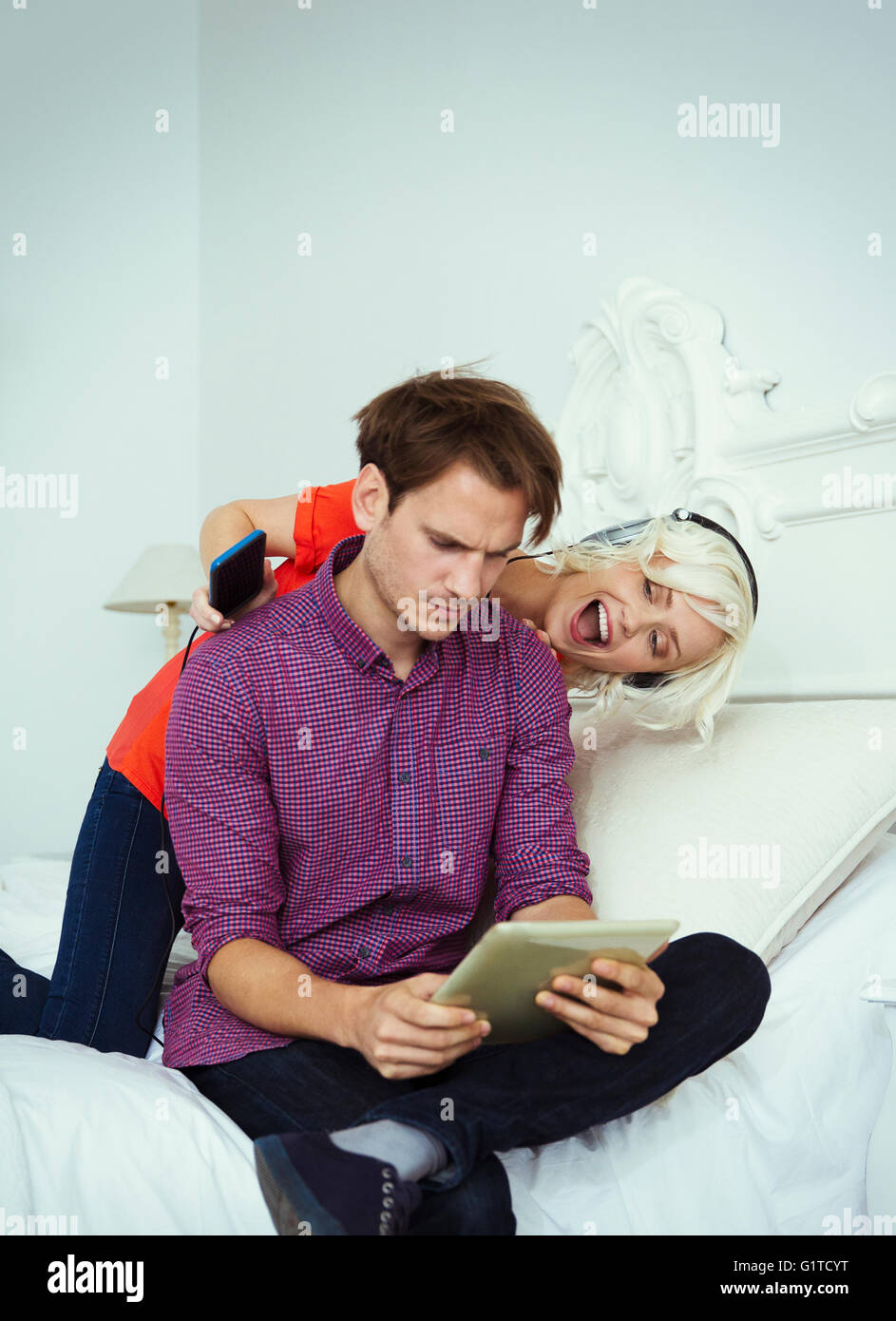 Juguetón esposa con auriculares y reproductor mp3 detrás del marido con la tableta digital Foto de stock