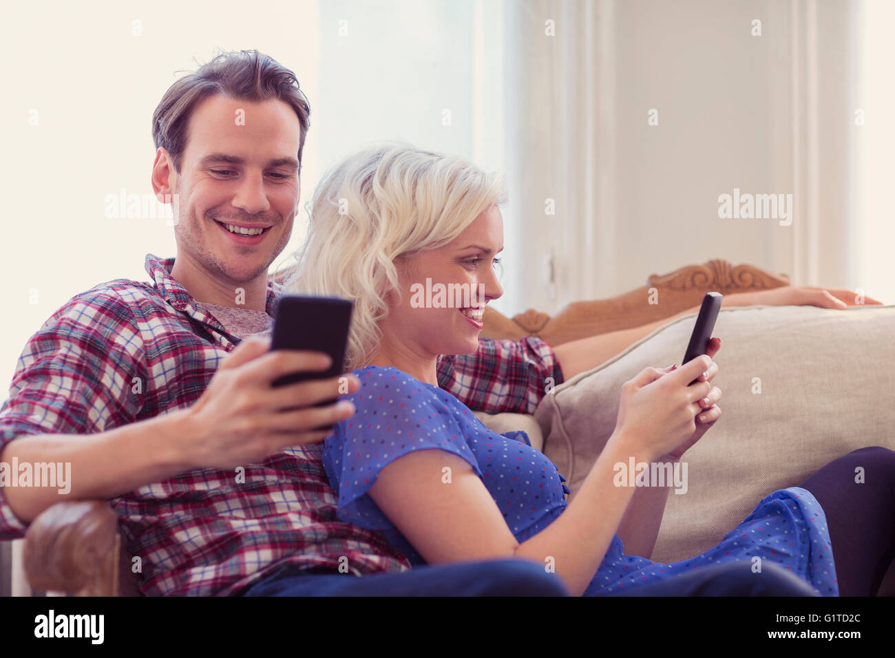 Par de texto con teléfonos celulares en la sala de sofá Foto de stock