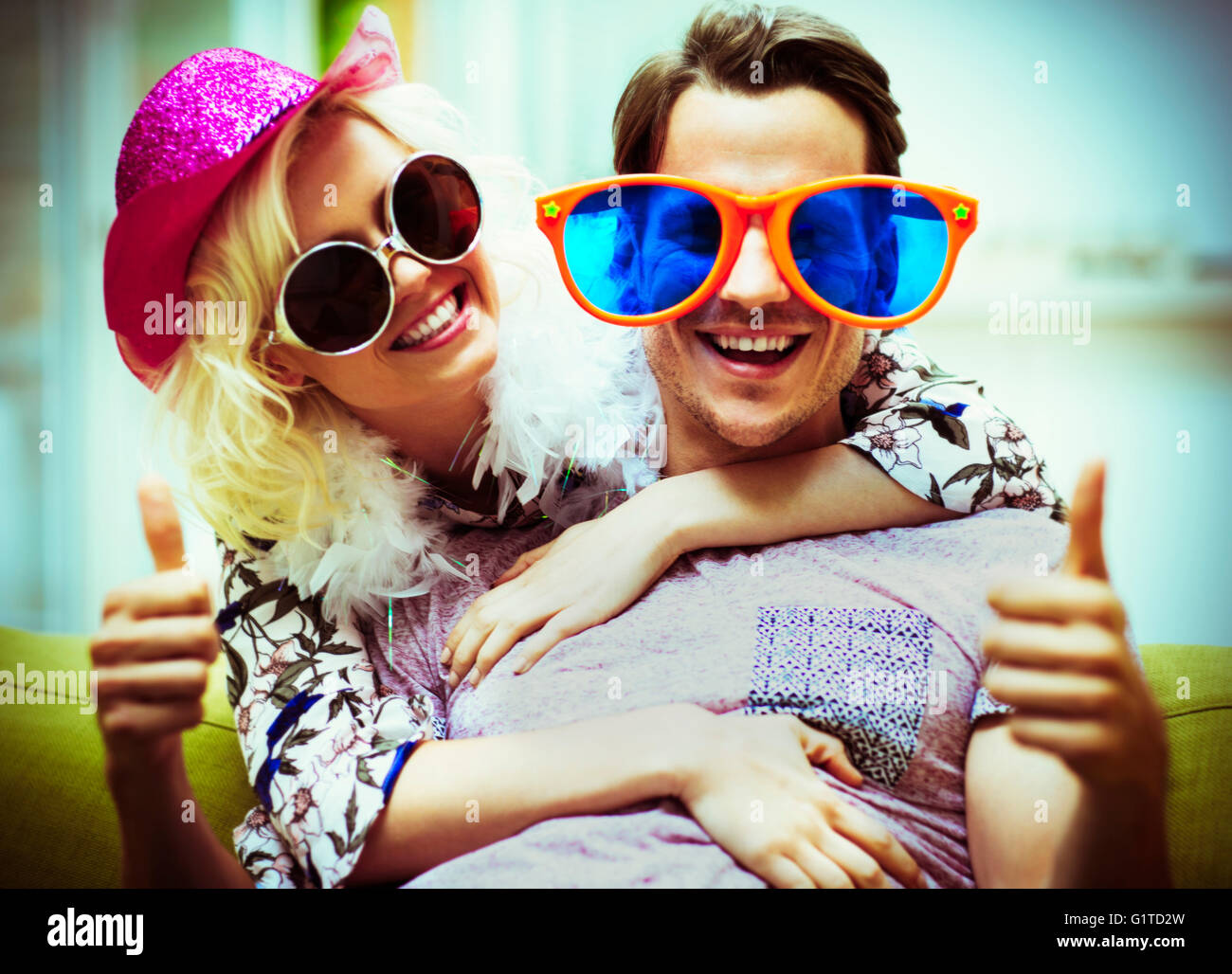 Retrato juguetón par llevar gafas de sol y un sombrero de disfraz gesticulando pulgares arriba Foto de stock