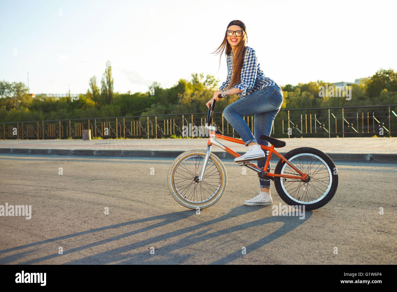 Encantadora mujer joven en un sombrero a montar una bicicleta en la ciudad en el fondo la luz solar exterior. Las personas activas Foto de stock