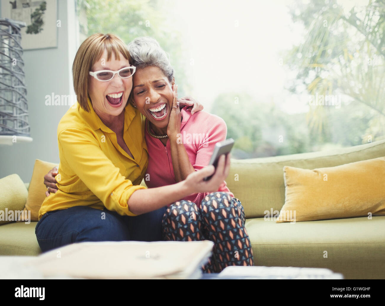 Laughing mujeres maduras abrazarse y teniendo selfie en el sofá Foto de stock