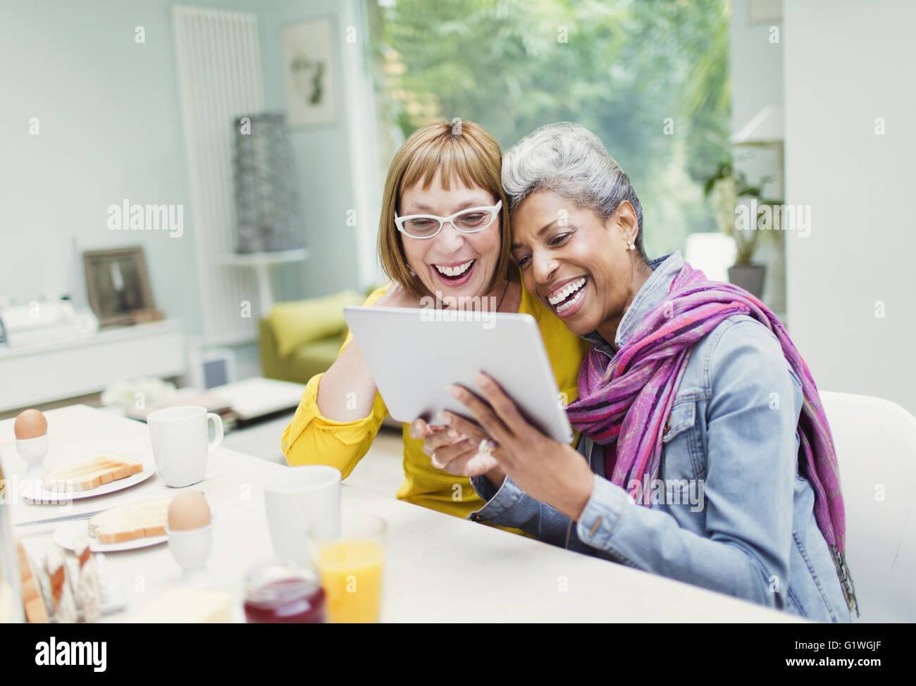Laughing mujeres maduras compartir en la mesa de desayuno de tableta digital Foto de stock