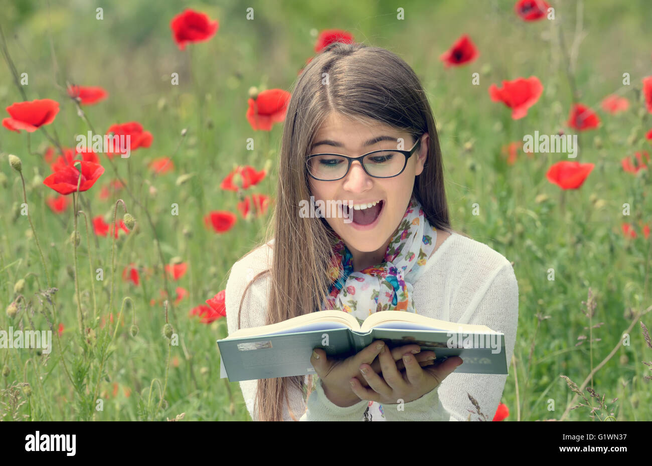 Adolescente a leer un libro en el campo de amapolas Foto de stock